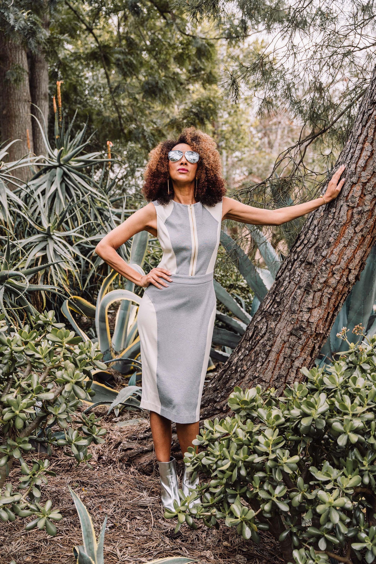 A woman in a vibrant pink sharply tailored pantsuit strides along a garden path